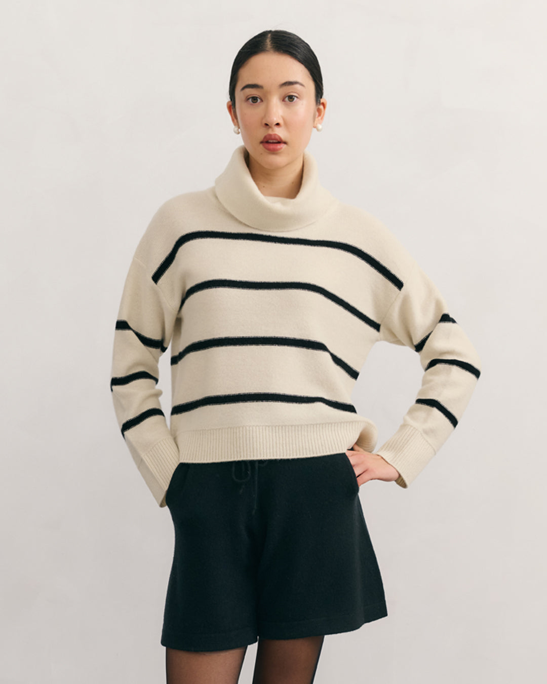 Model wearing Cashmerism Cream Raw 100% cashmere striped fold neck turtleneck pullover jumper with black shorts.