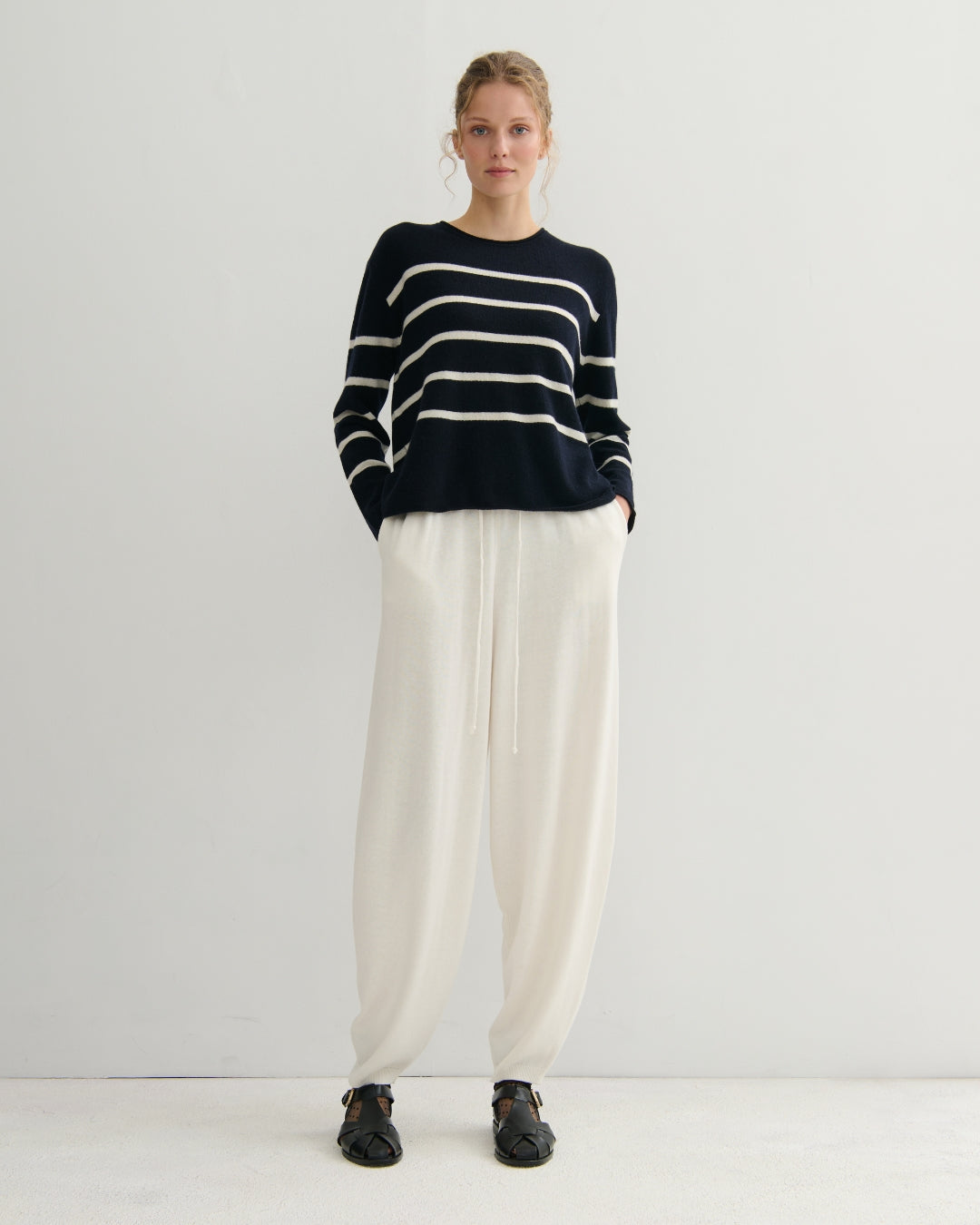 Person wearing a navy and white striped sweater with cream pants on a white background