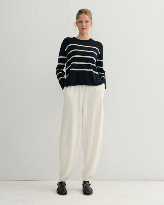 Person wearing a navy and white striped sweater with cream pants on a white background